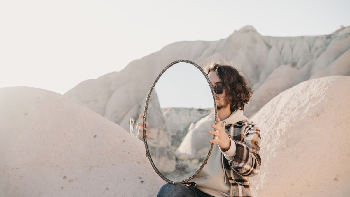 A person holding a mirror in a rocky desert landscape, capturing reflections creatively.